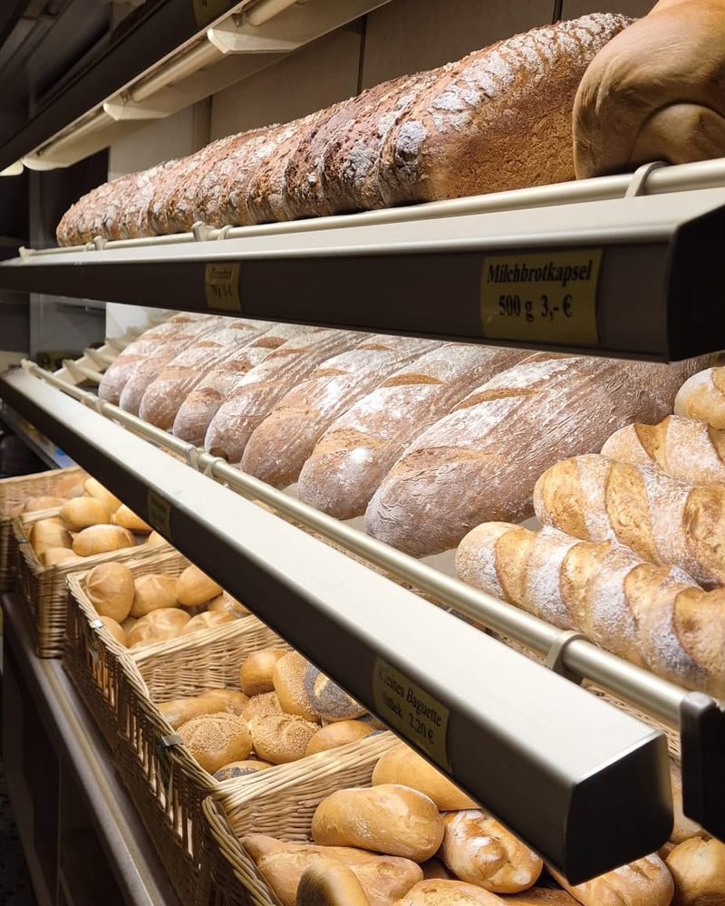 Regal mit frischen Broten, Baguettes und Körben voller Brötchen im Verkaufsraum.