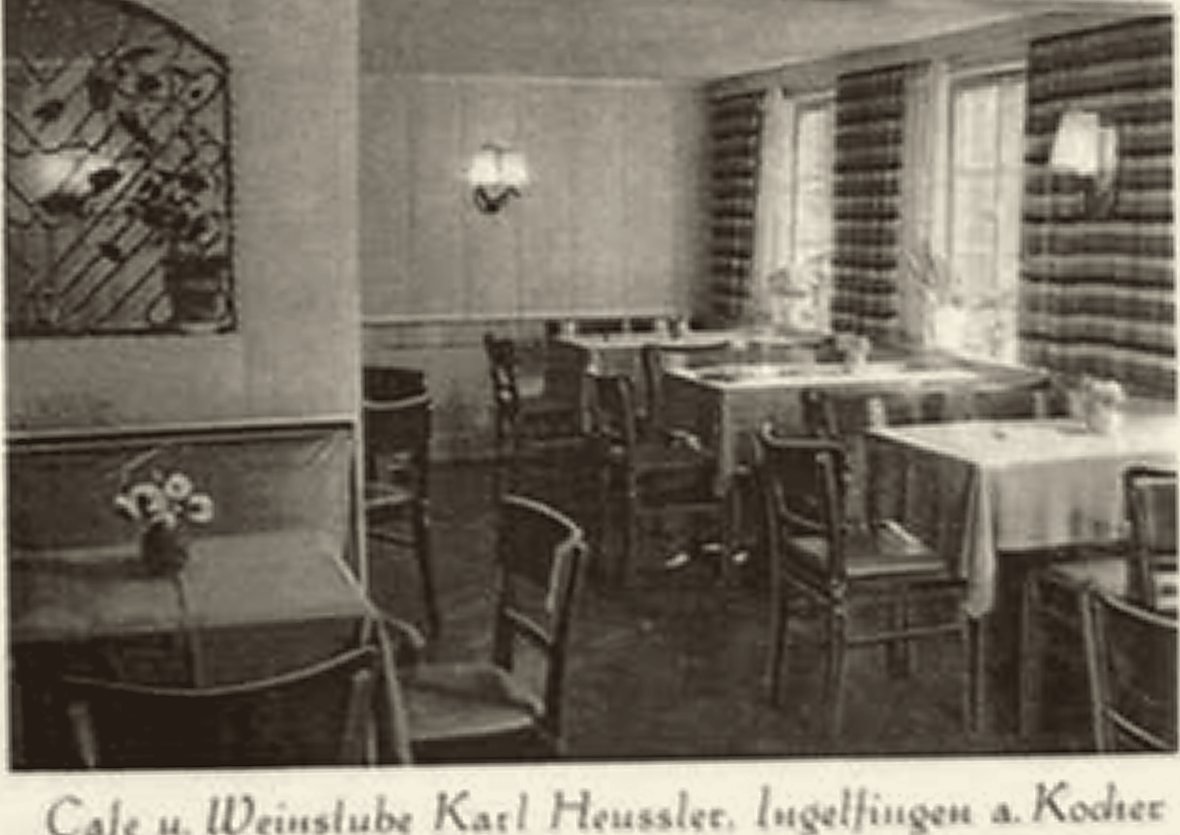 Gaststube mit eingedeckten Tischen, Holzstühlen und Wandleuchten.
