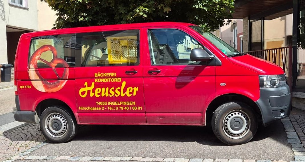 Der rote Lieferwagen der Bäckerei Heussler mit Brezel-Logo und Schriftzug, geparkt vor dem Laden in der Hirschgasse.